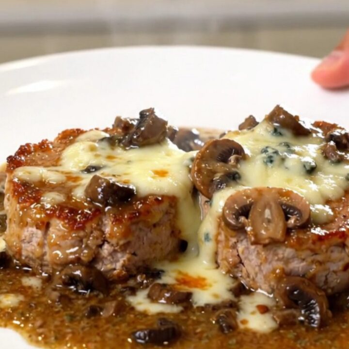 A close-up of creamy blue cheese pork tenderloin medallions on a white plate.