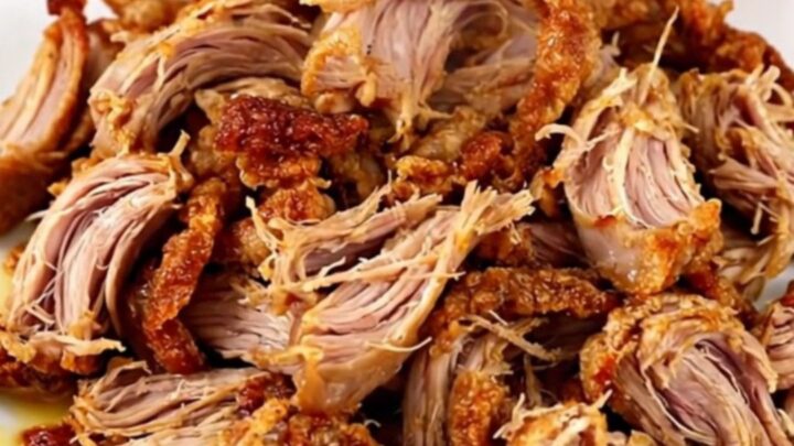 A slow cooker filled with tender, citrus-spiced pork carnitas chunks ready to be shredded.