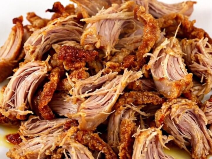 A slow cooker filled with tender, citrus-spiced pork carnitas chunks ready to be shredded.