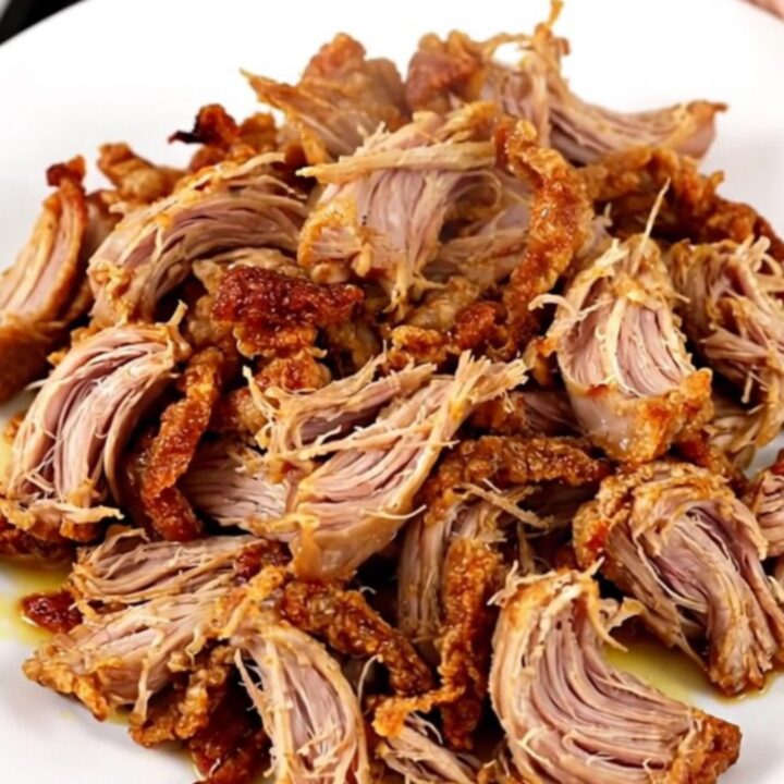 A slow cooker filled with tender, citrus-spiced pork carnitas chunks ready to be shredded.