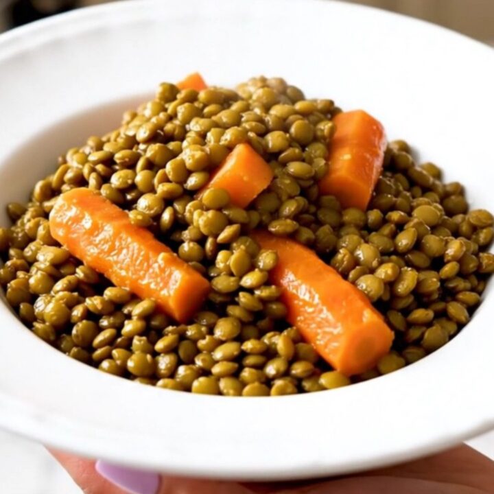 A close-up of a bowl filled with slow-cooked green lentils, carrots, and onions in a savory, glossy mustard broth.