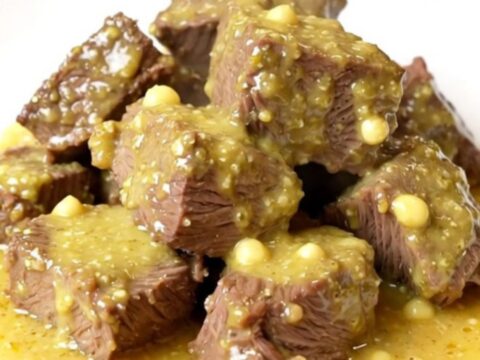 A close-up of tender beef chunks smothered in a creamy, glossy Dijon and mushroom sauce on a white plate.