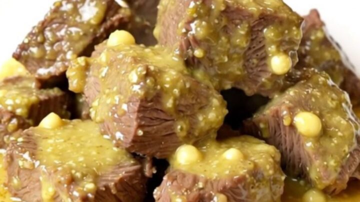 A close-up of tender beef chunks smothered in a creamy, glossy Dijon and mushroom sauce on a white plate.