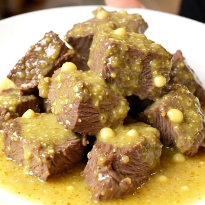 A close-up of tender beef chunks smothered in a creamy, glossy Dijon and mushroom sauce on a white plate.