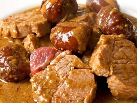 A steaming plate of slow-cooked pork shoulder pieces and glazed chestnuts in a rich, creamy sauce.
