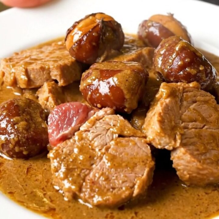 A steaming plate of slow-cooked pork shoulder pieces and glazed chestnuts in a rich, creamy sauce.