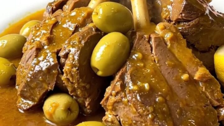 Slow cooker veal tagine served on a white plate with visible olives and preserved lemon wedges.