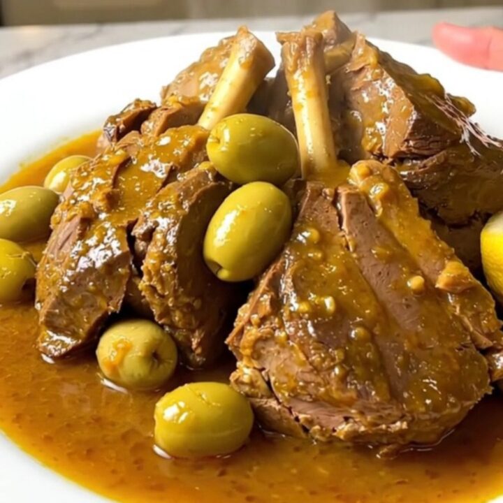 Slow cooker veal tagine served on a white plate with visible olives and preserved lemon wedges.