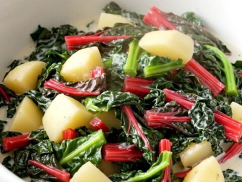 A rustic bowl filled with creamy diced potatoes and vibrant green Swiss chard in a rich, glossy cream sauce.