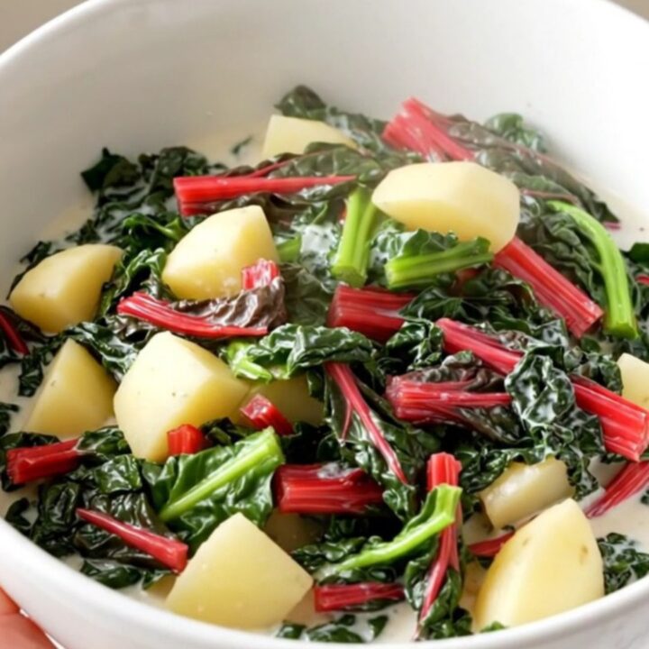 A rustic bowl filled with creamy diced potatoes and vibrant green Swiss chard in a rich, glossy cream sauce.