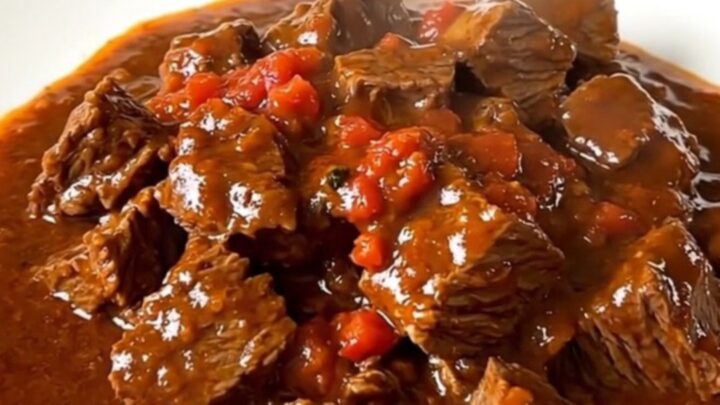 A close-up of a steaming, rich Sète-style beef stew served in a white bowl with a glossy tomato wine sauce.