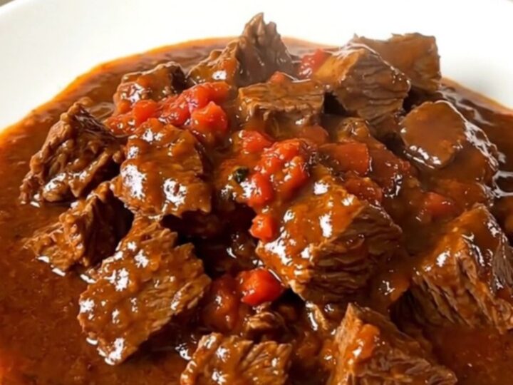 A close-up of a steaming, rich Sète-style beef stew served in a white bowl with a glossy tomato wine sauce.