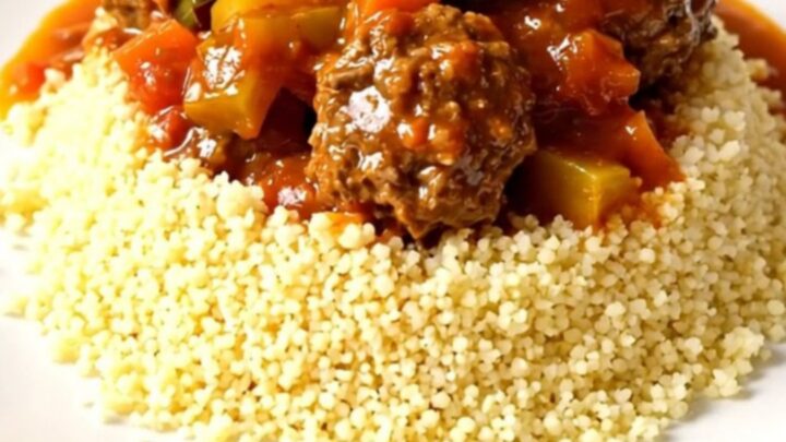 A rustic bowl of slow-cooked beef meatballs and vegetables in a rich tomato sauce served over a bed of fluffy couscous.