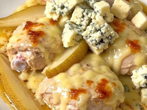 A close-up of tender chicken thighs coated in a rich, creamy Fourme d'Ambert blue cheese sauce with pear wedges.