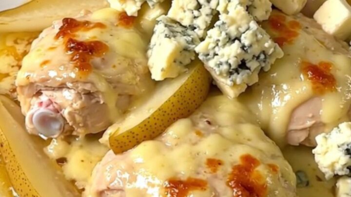 A close-up of tender chicken thighs coated in a rich, creamy Fourme d'Ambert blue cheese sauce with pear wedges.