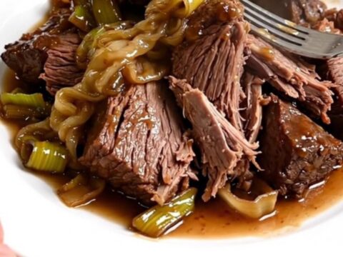 Slow cooker filled with braised beef chunks and melted leeks in a rich sauce.