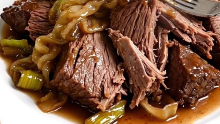 Slow cooker filled with braised beef chunks and melted leeks in a rich sauce.