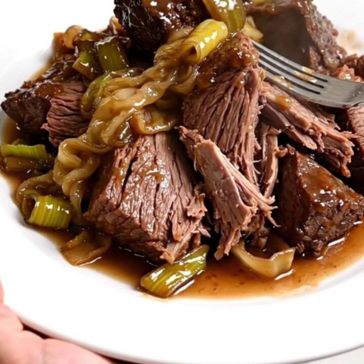 Slow cooker filled with braised beef chunks and melted leeks in a rich sauce.
