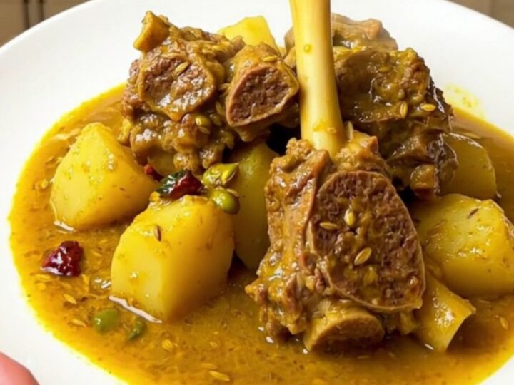 A white round plate filled with tender, steaming lamb colombo stew with chunks of potato.