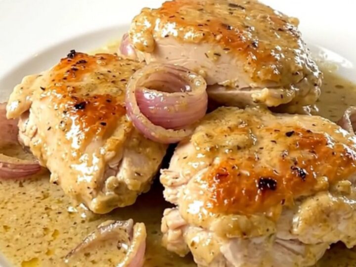 A rustic, creamy chicken dish with tender shallots served on a white plate.