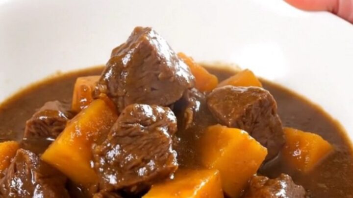 Ragoût de bœuf tendre servi dans une assiette blanche avec des morceaux de potimarron.