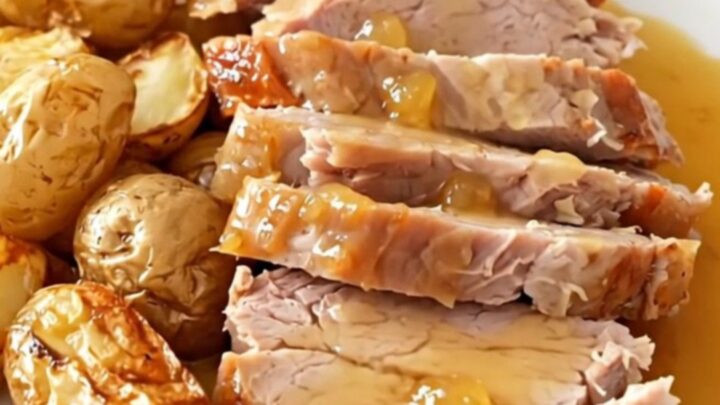 A rustic slow cooker pork roast served with golden baby potatoes and a glossy cider sauce on a white plate.