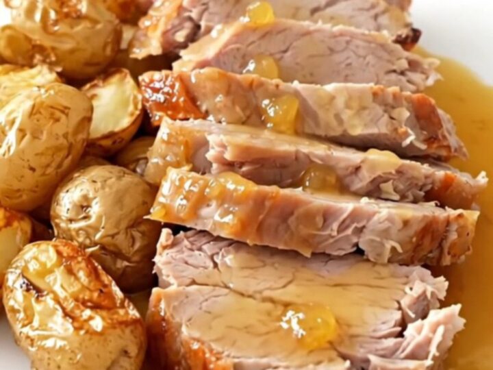 A rustic slow cooker pork roast served with golden baby potatoes and a glossy cider sauce on a white plate.