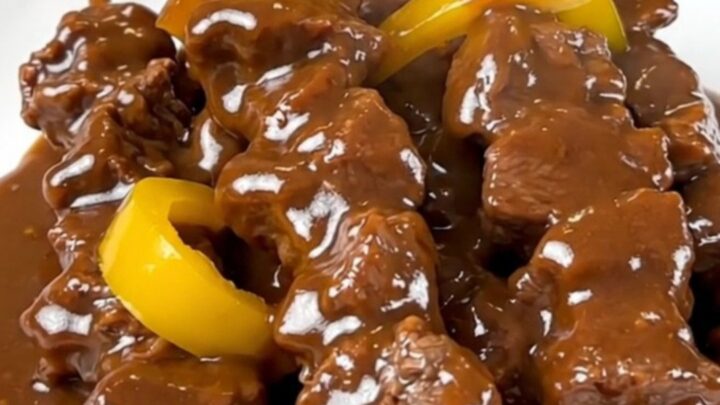 A close-up of slow cooker satay beef served on a white plate with a glossy coconut sauce.