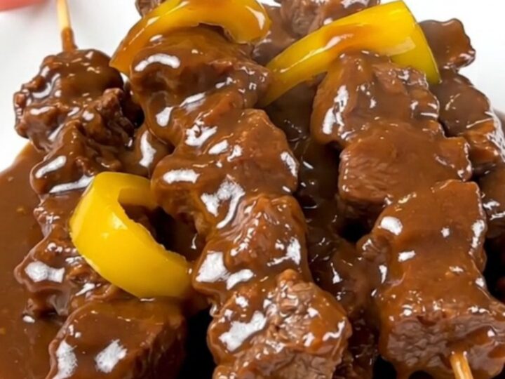 A close-up of slow cooker satay beef served on a white plate with a glossy coconut sauce.