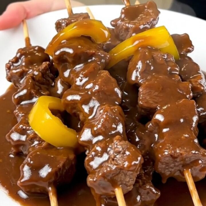 A close-up of slow cooker satay beef served on a white plate with a glossy coconut sauce.