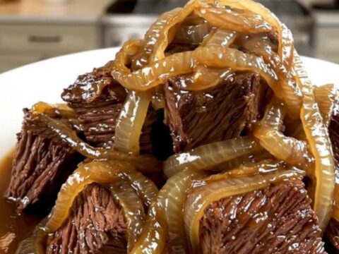 A close-up of glossy, tender braised beef neck with melting red onions served on a white plate.