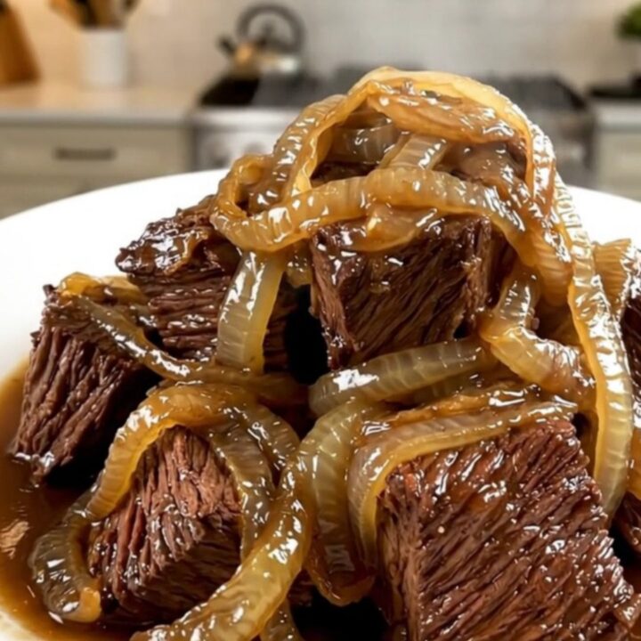 A close-up of glossy, tender braised beef neck with melting red onions served on a white plate.