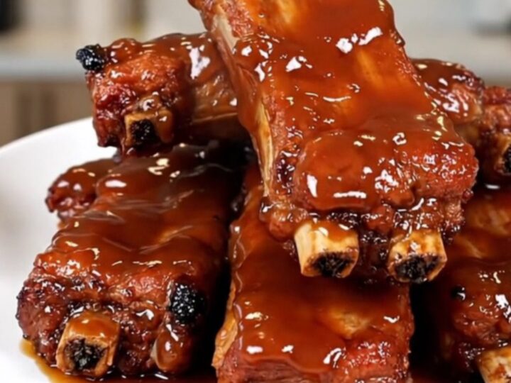Travers de porc caramélisés et fondants servis dans une assiette blanche avec une sauce brillante.