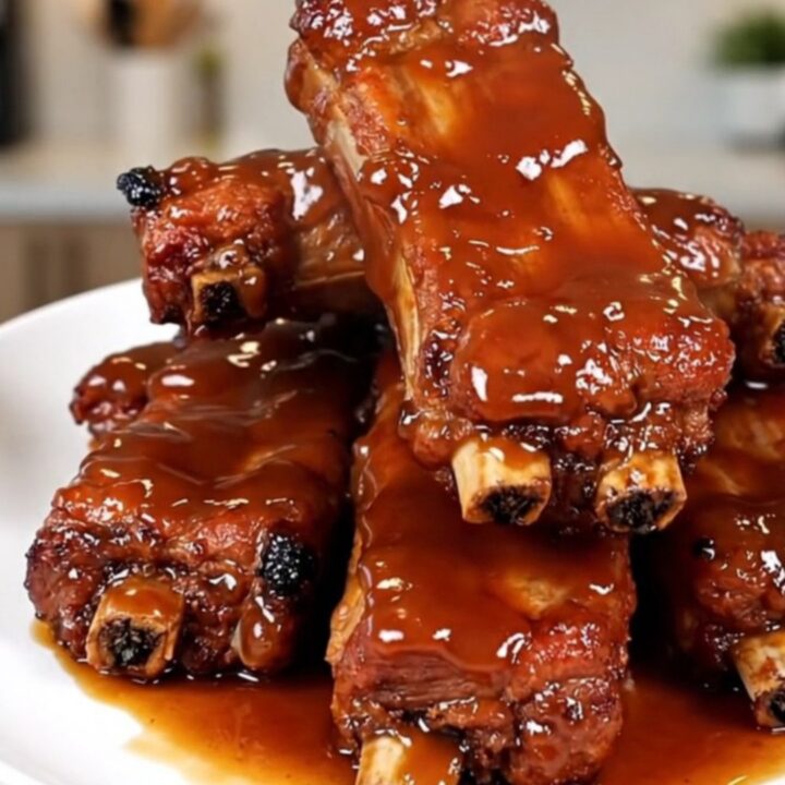 Travers de porc caramélisés et fondants servis dans une assiette blanche avec une sauce brillante.