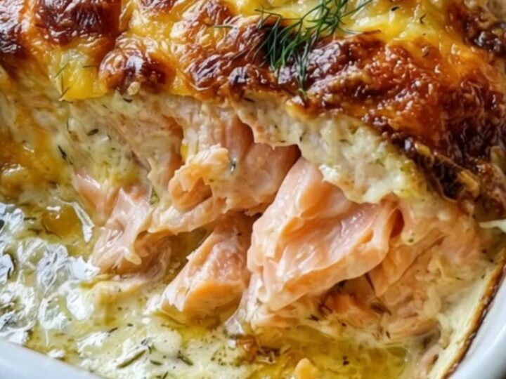 A white baking dish filled with creamy baked salmon topped with a golden-brown bubbly cheese crust and fresh dill.