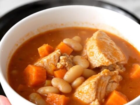 A white bowl filled with steaming chicken and white bean stew on a speckled quartz countertop.