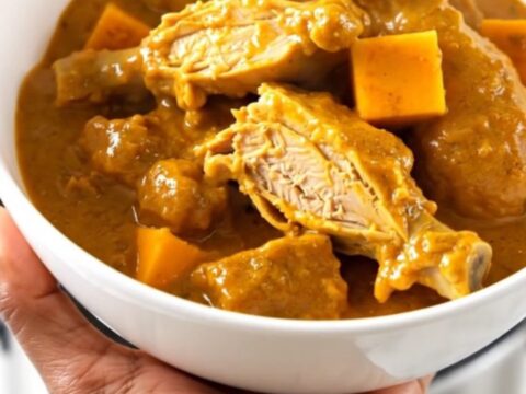 A slow cooker filled with raw turkey, red kuri squash, and coconut milk ready to be cooked.