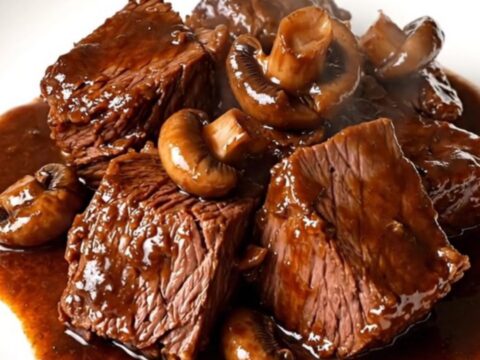 A rustic bowl of slow-cooked braised beef with sliced mushrooms and a rich, glossy red wine sauce.