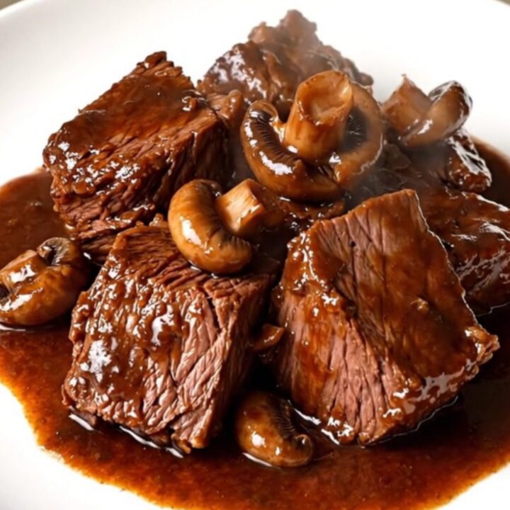 A rustic bowl of slow-cooked braised beef with sliced mushrooms and a rich, glossy red wine sauce.