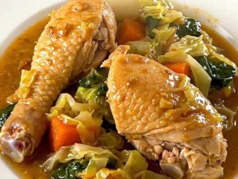 Slow cooker chicken and cabbage stew in a black oval pot on a speckled countertop.