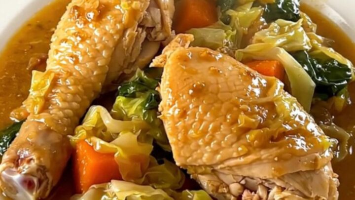 Slow cooker chicken and cabbage stew in a black oval pot on a speckled countertop.