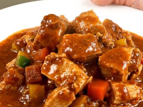 A steaming bowl of turkey peanut stew served on a white plate with a rich, glossy sauce.