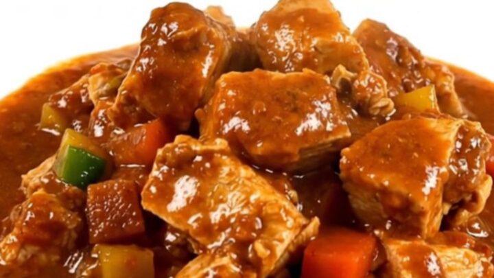 A steaming bowl of turkey peanut stew served on a white plate with a rich, glossy sauce.