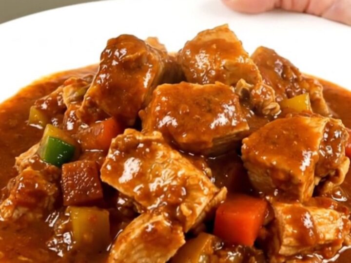 A steaming bowl of turkey peanut stew served on a white plate with a rich, glossy sauce.
