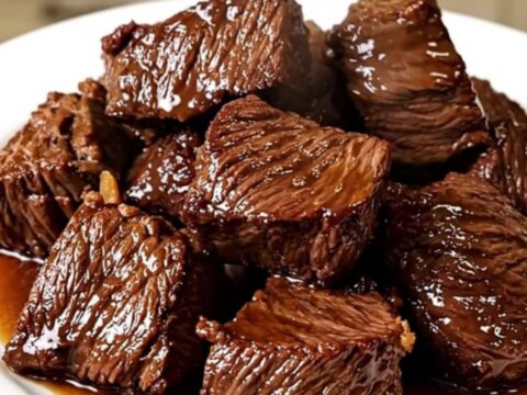 A close-up of tender, dark, glossy beef chunks in a rich sauce served on a white plate.