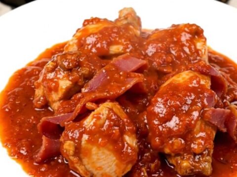 A top-down view of a black slow cooker on a speckled quartz countertop filled with chicken, ham, and tomatoes.