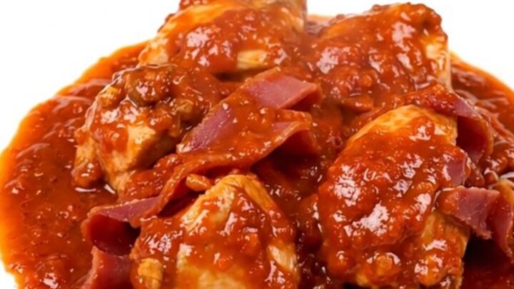 A top-down view of a black slow cooker on a speckled quartz countertop filled with chicken, ham, and tomatoes.