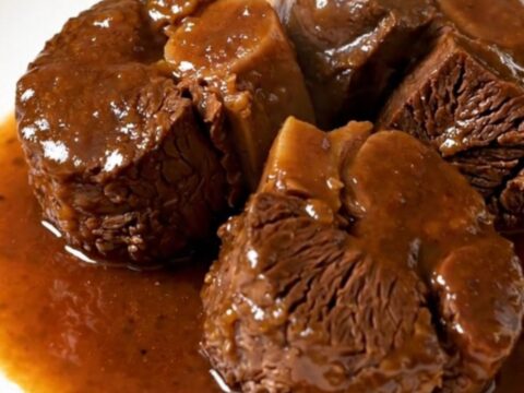 A close-up of tender, braised beef cheeks served on a white plate with carrots and a rich, glossy sauce.
