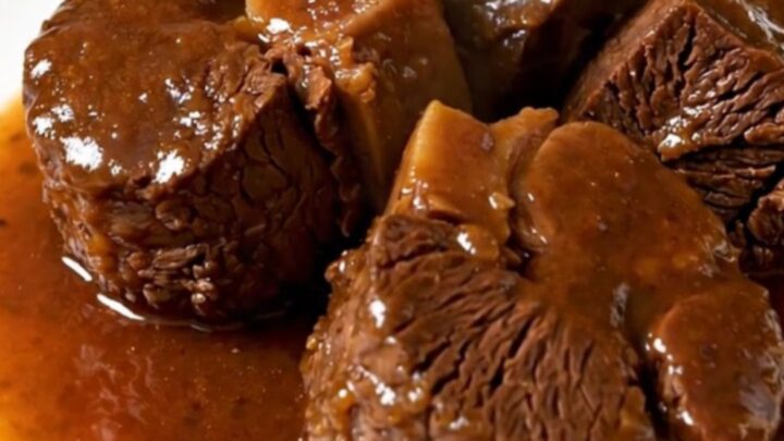 A close-up of tender, braised beef cheeks served on a white plate with carrots and a rich, glossy sauce.