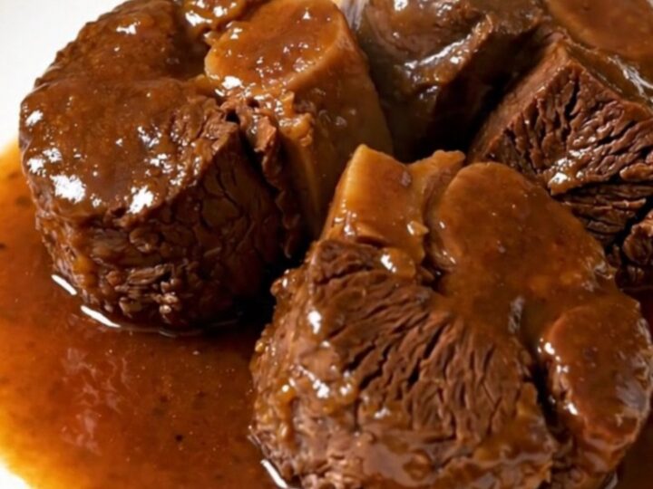 A close-up of tender, braised beef cheeks served on a white plate with carrots and a rich, glossy sauce.